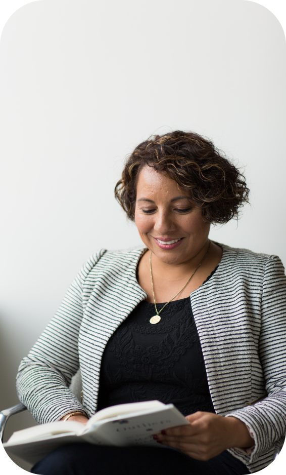 Photographie d'une personne souriante, habillée d'une veste de tailleur rayée noir et blanc, qui consulte un livre, posé sur ses genoux